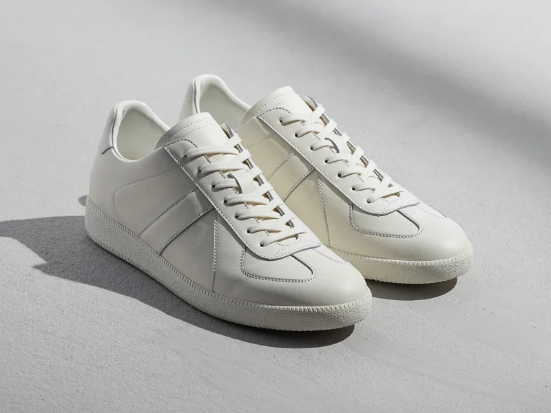 Weisser Low-Top-Leder-Sneaker im Dreiviertelblick auf hellem Beton, als Konzeptillustration.