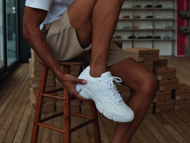 Person probiert auf einem niedrigen Holzhocker einen Sneaker an, im Hintergrund schlichte Kartons.